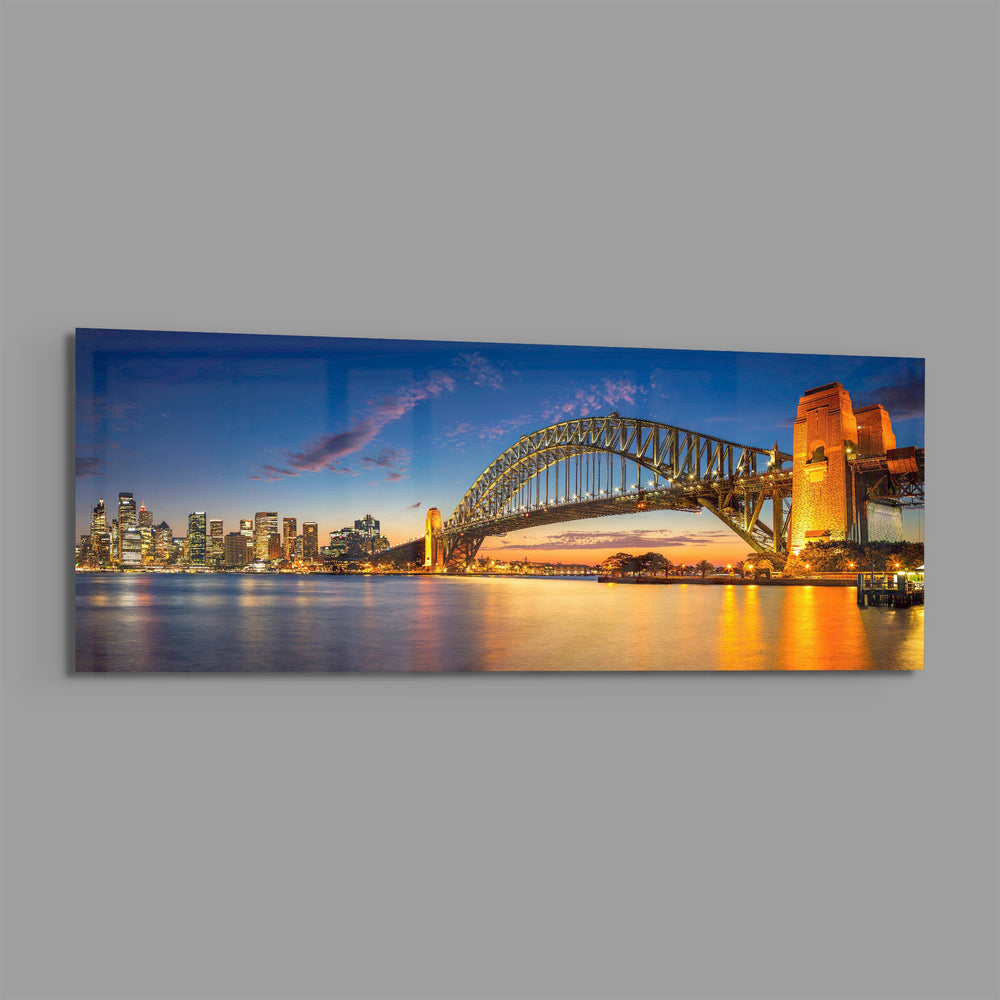 Panoramic harbor city at dusk, a great steel arch bridge lit gold beside a glittering downtown skyline mirrored in calm water. panoramic glass wall art E