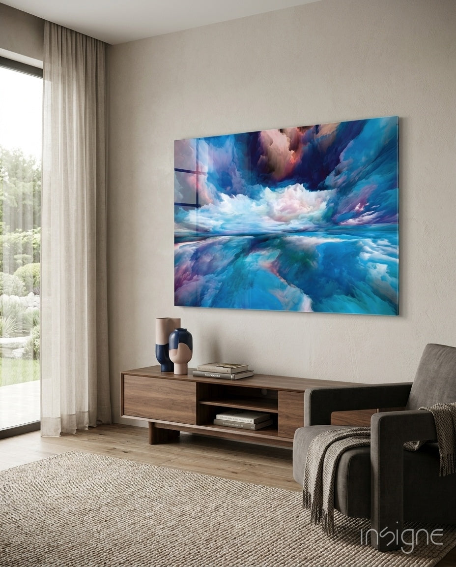 Blue Explosion glass wall art displayed above a wood credenza in a soft white-plaster lounge with charcoal armchair and pampas vase