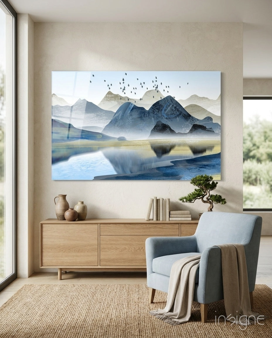 Mountains glass wall art displayed above a wood credenza in a soft cream-plaster lounge with pale blue armchair and bonsai
