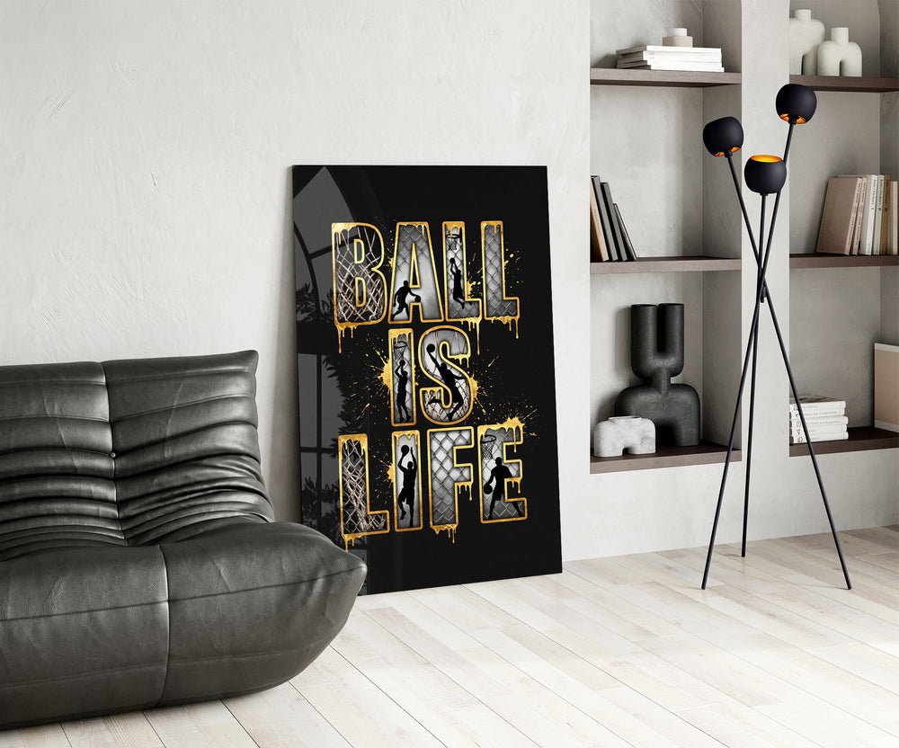 gold Ball Is Life basketball typography glass wall art leaning beside a dark leather sofa