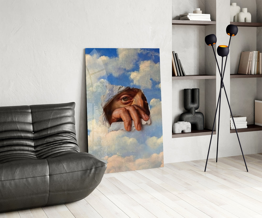 an eye and hand breaking through a painted sky glass wall art leaning beside a dark leather sofa