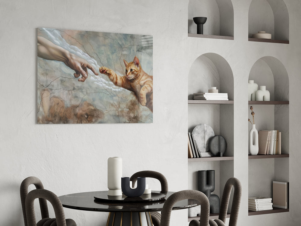 ginger kitten reaching a paw to a human hand glass wall art leaning beside a dark leather sofa