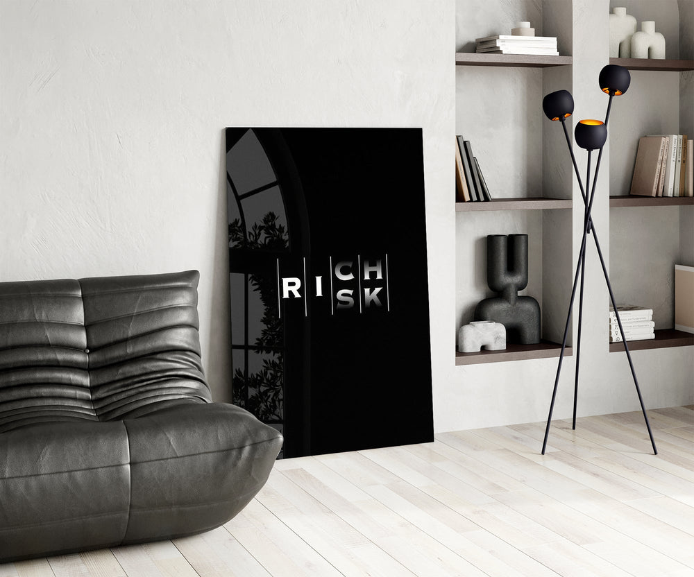 interlocking rich and risk typography glass wall art leaning beside a dark leather sofa