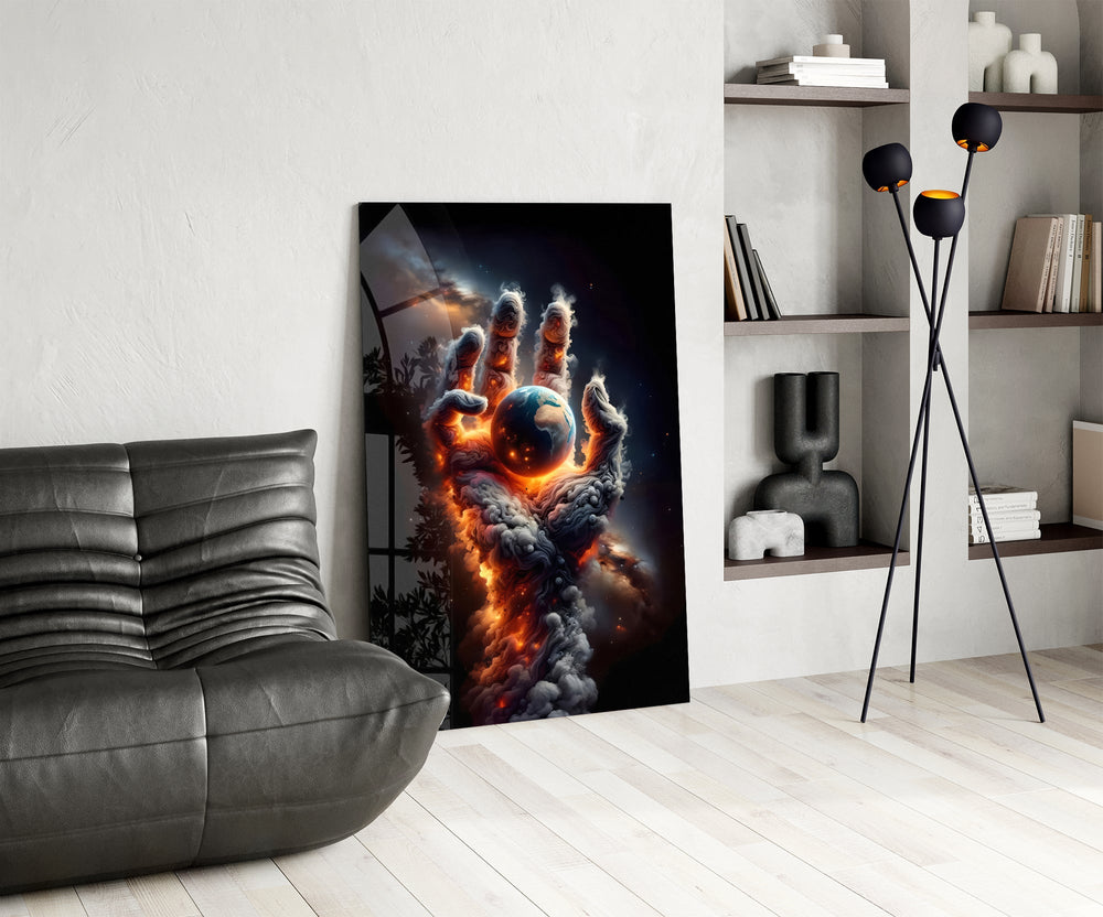 a hand of smoke and fire cradling planet earth glass wall art leaning beside a dark leather sofa