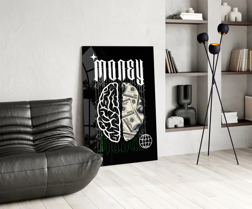 a brain half built from hundred-dollar bills glass wall art leaning beside a dark leather sofa