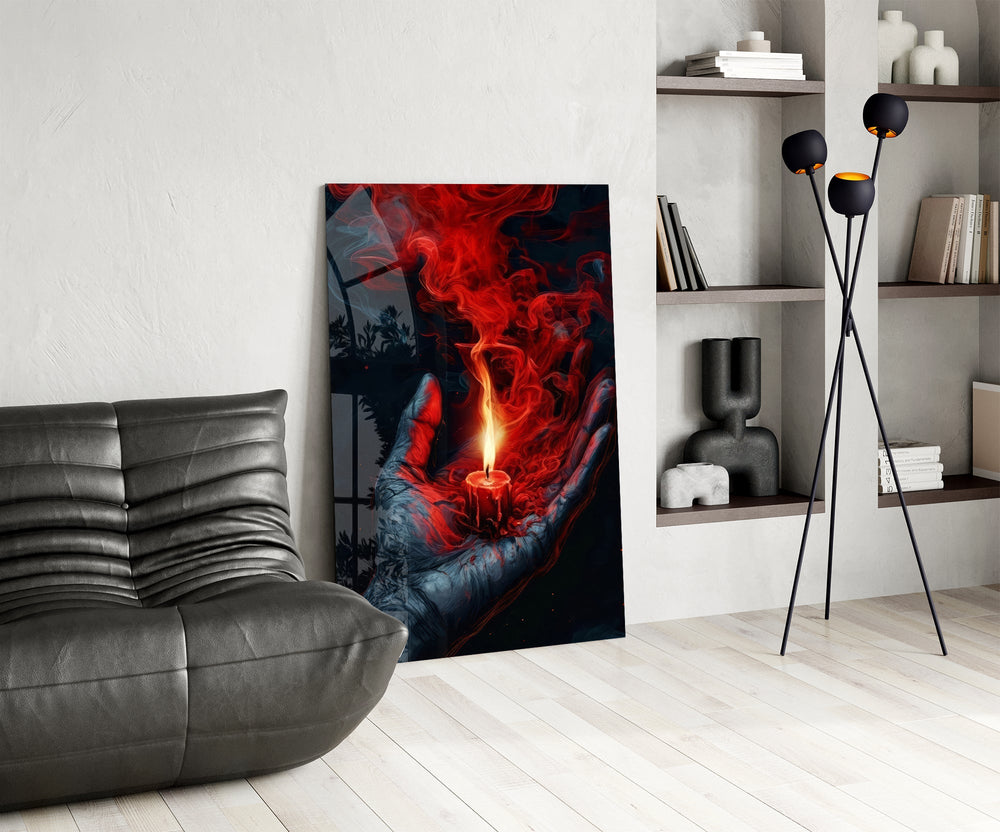 a cupped hand holding a burning red candle glass wall art leaning beside a dark leather sofa