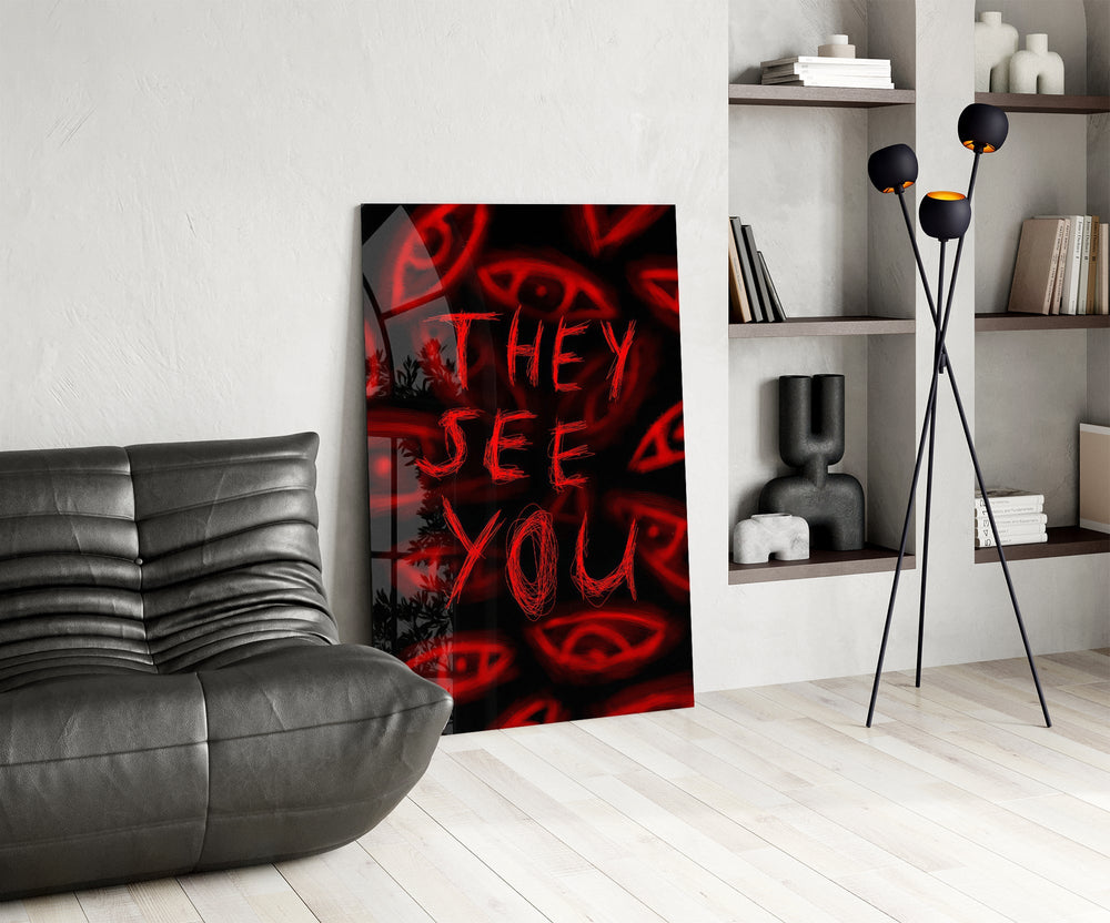 a red handwritten warning over watching eyes glass wall art leaning beside a dark leather sofa