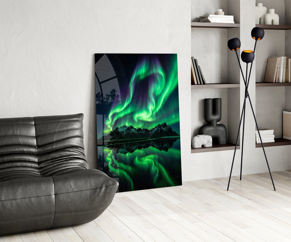 a green aurora over mirrored peaks glass wall art leaning beside a dark leather sofa