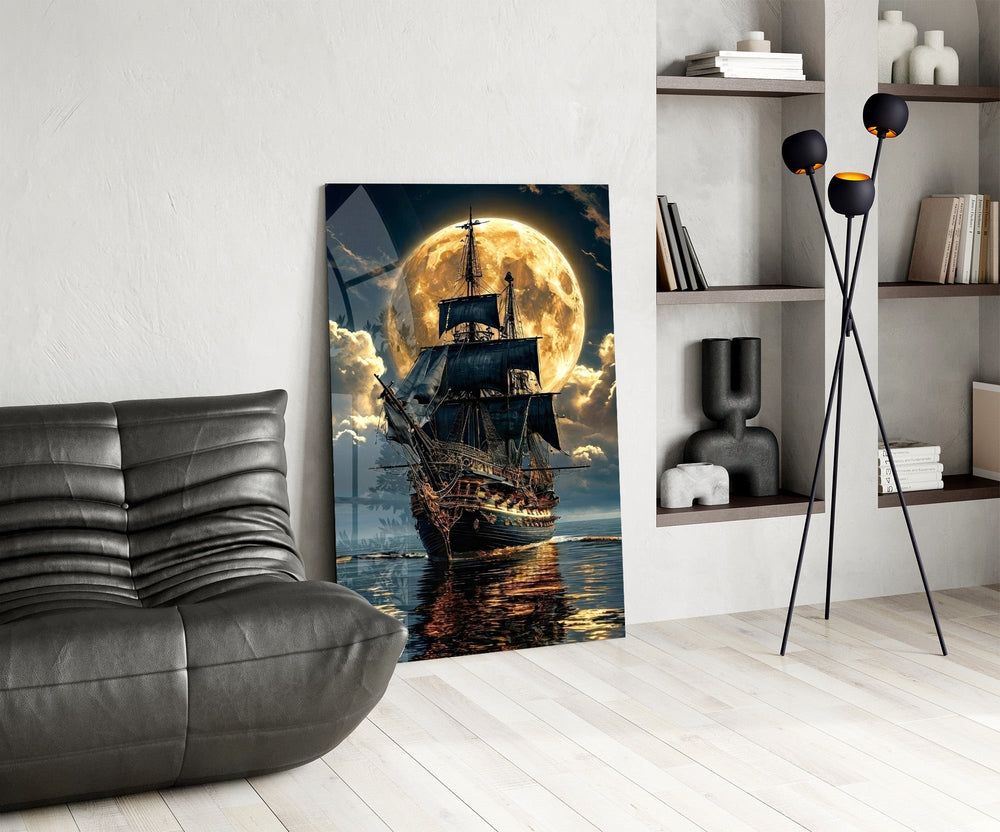 tall sailing ship before a full moon glass wall art leaning beside a dark leather sofa