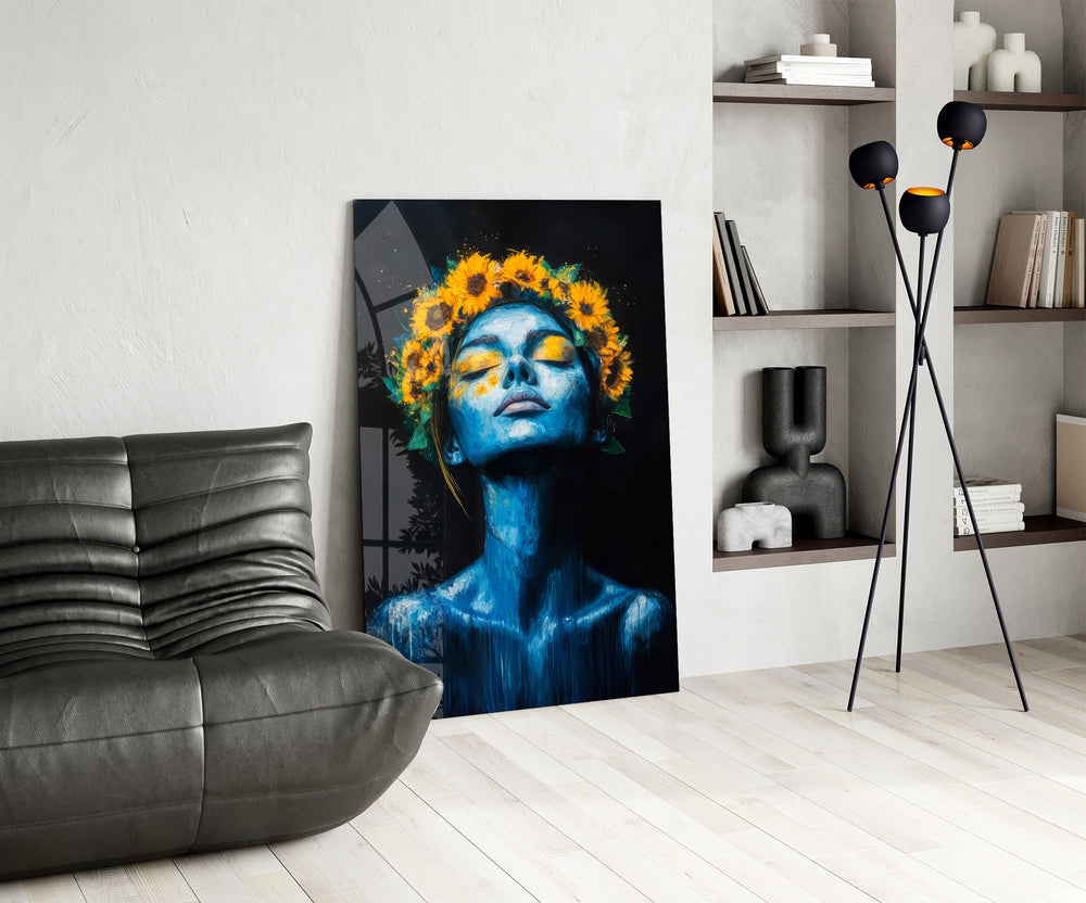 a blue-skinned woman crowned with sunflowers glass wall art leaning beside a dark leather sofa