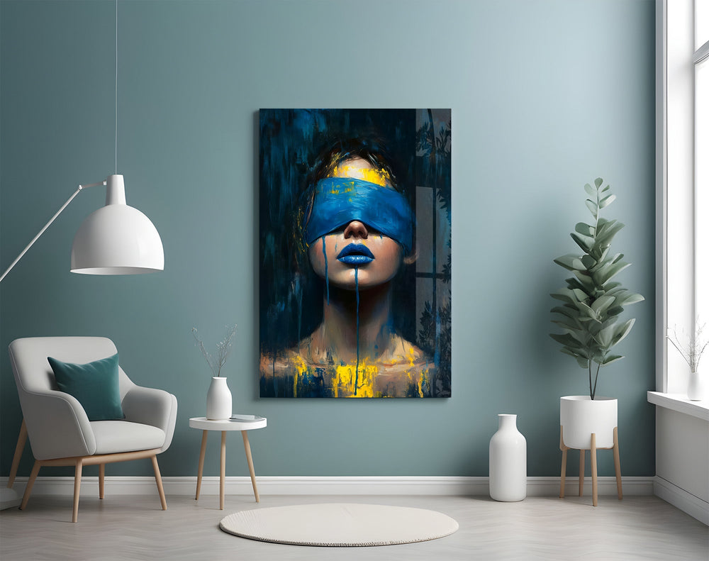 a blindfolded woman with blue lips and dripping paint glass wall art styled above an armchair in a reading corner