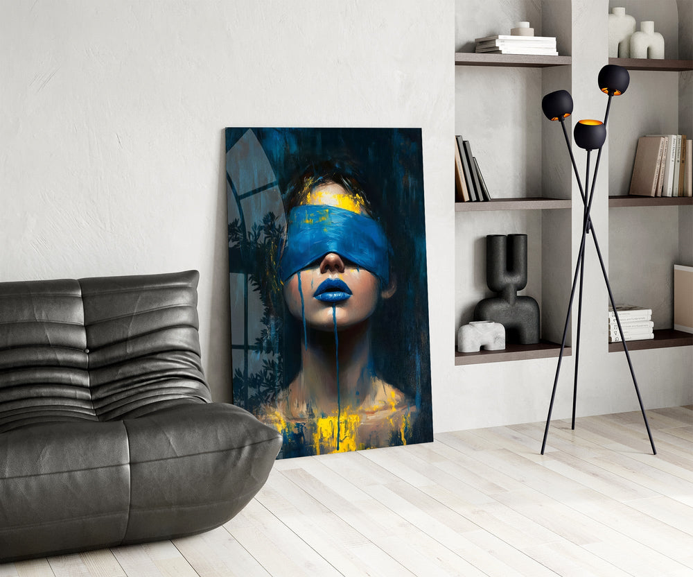 a blindfolded woman with blue lips and dripping paint glass wall art leaning beside a dark leather sofa