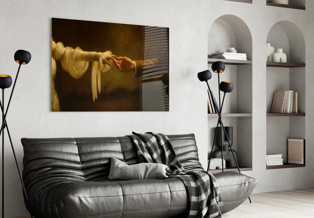 two hands reaching in golden light glass wall art styled above an armchair in a reading corner