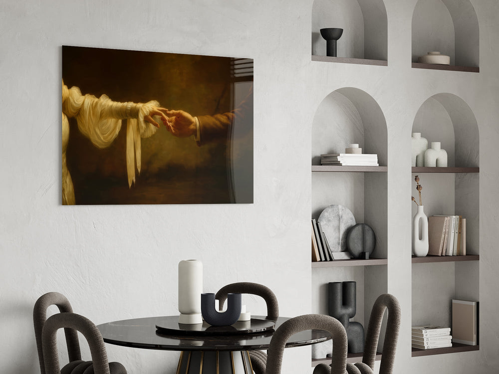 two hands reaching in golden light glass wall art leaning beside a dark leather sofa