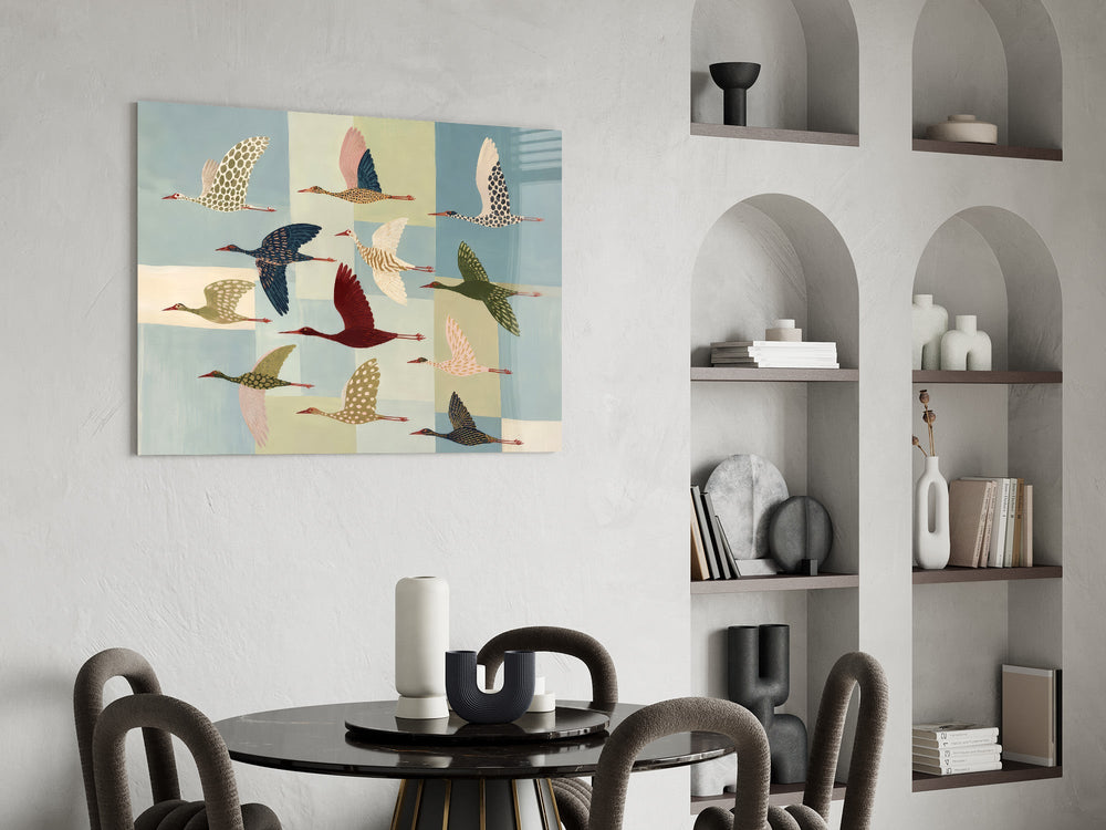 a flock of stylized cranes in flight glass wall art leaning beside a dark leather sofa