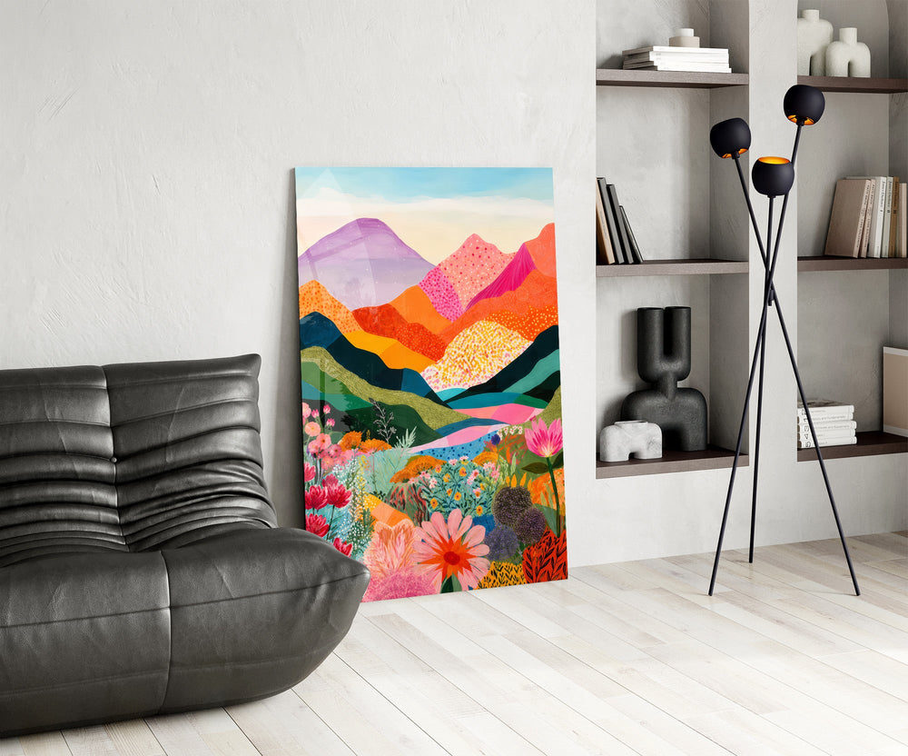colorful layered mountains above a flower valley glass wall art leaning beside a dark leather sofa