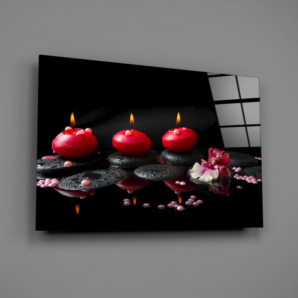Close-up detail of red candles, black stones, and orchid in still reflection