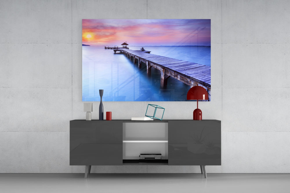 Fine art photography – weathered wooden dock stretching over still tropical water beneath pastel pink, orange and purple sunset sky
