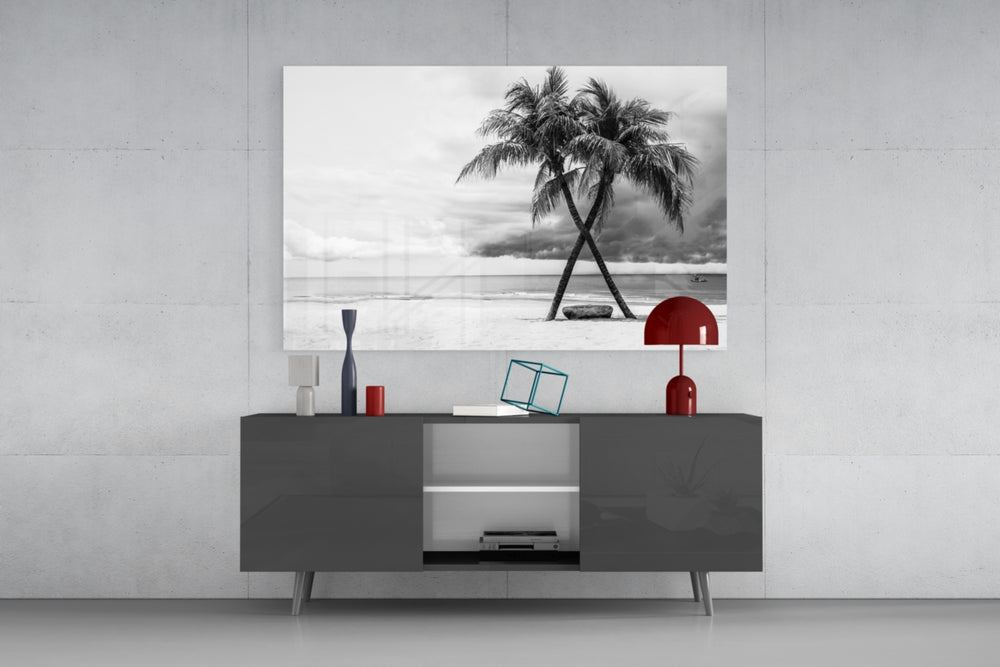 Fine art black and white photography – two leaning palm trees crossing gracefully on white sandy beach, dramatic cloudy coastal sky
