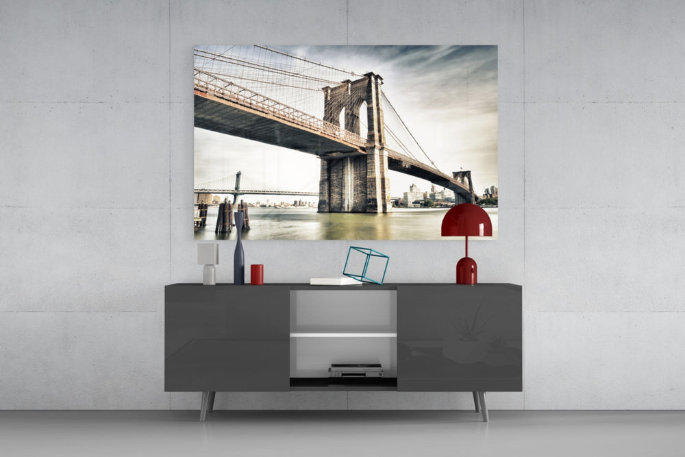 Fine art long exposure photography – Brooklyn Bridge stone tower and steel cables in warm muted tones over mirror-calm East River