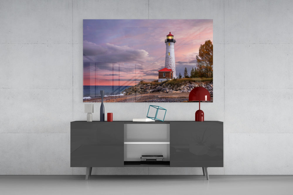Fine art photography – white lighthouse with glowing lamp on rocky Great Lakes shore at pink and lavender sunset with autumn foliage