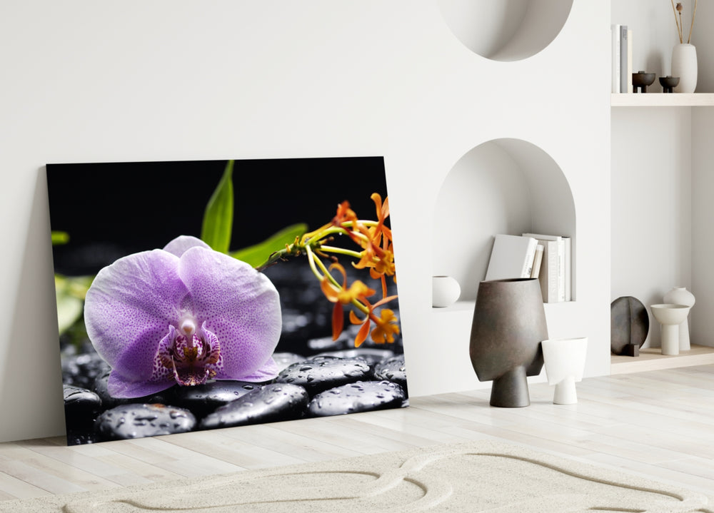 Close-up detail of the purple orchid and orange bloom on wet stones