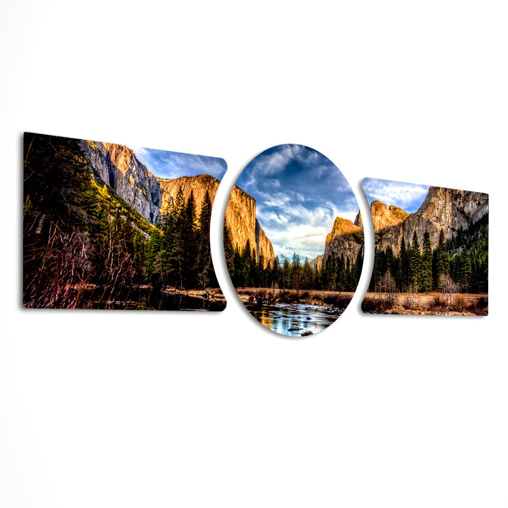 A panoramic mountain valley with golden-lit granite cliffs, a winding river, and a dense pine forest under a dramatic blue sky. 3 piece glass wall art set D