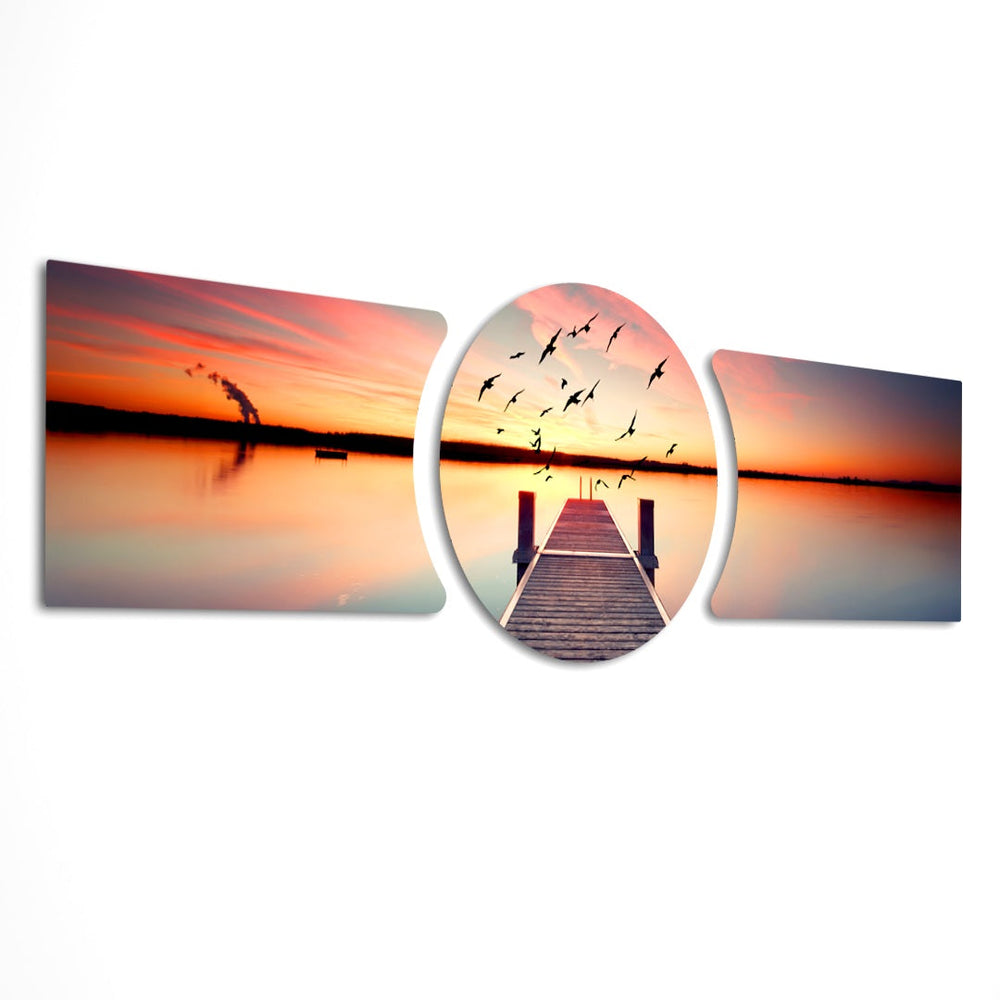 A wooden pier reaching into a calm lake at sunset with a flock of birds taking flight across a fiery orange sky. 3 piece glass wall art set E