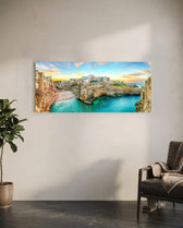 A cliffside Mediterranean town glowing at sunset above a turquoise cove. panoramic glass wall art C