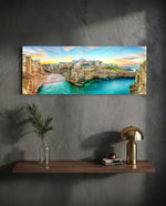 A cliffside Mediterranean town glowing at sunset above a turquoise cove. panoramic glass wall art D
