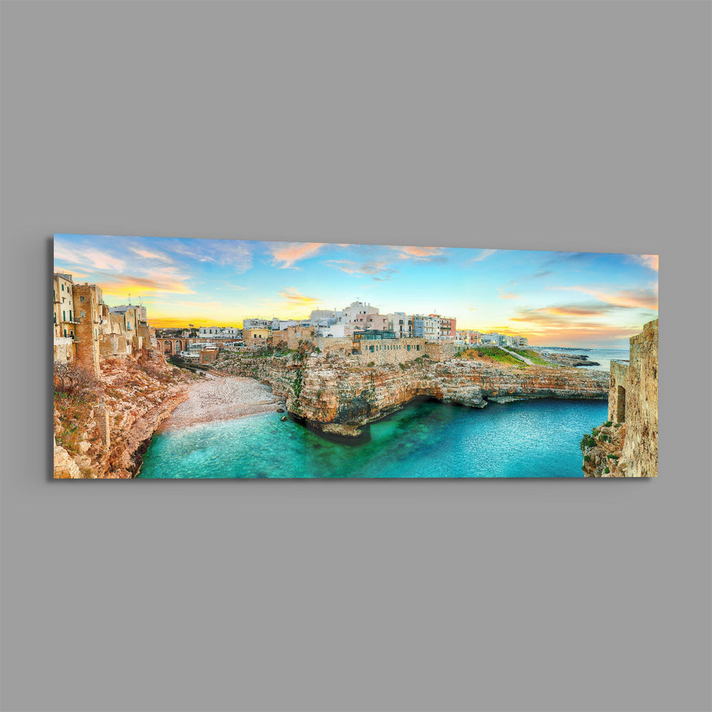 A cliffside Mediterranean town glowing at sunset above a turquoise cove. panoramic glass wall art E