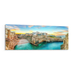 A cliffside Mediterranean town glowing at sunset above a turquoise cove. panoramic glass wall art F