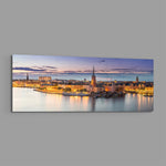 Panoramic Nordic old-town waterfront at dusk, warm street lights glowing along the quay beneath a soft pastel twilight sky. panoramic glass wall art E