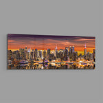 Panoramic metropolitan skyline at sunset, dense illuminated skyscrapers glowing beneath a fiery orange and violet sky, mirrored in the river below. panoramic glass wall art E