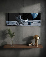 A spacesuited astronaut lounging in a deck chair on the lunar surface while planet Earth hangs in the black sky. panoramic glass wall art D