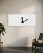 A single black chess pawn casting the long shadow of a king across a white textured surface, with a short motivational line of text panoramic glass wall art C