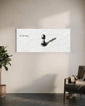 A single black chess pawn casting the long shadow of a king across a white textured surface, with a short motivational line of text panoramic glass wall art C