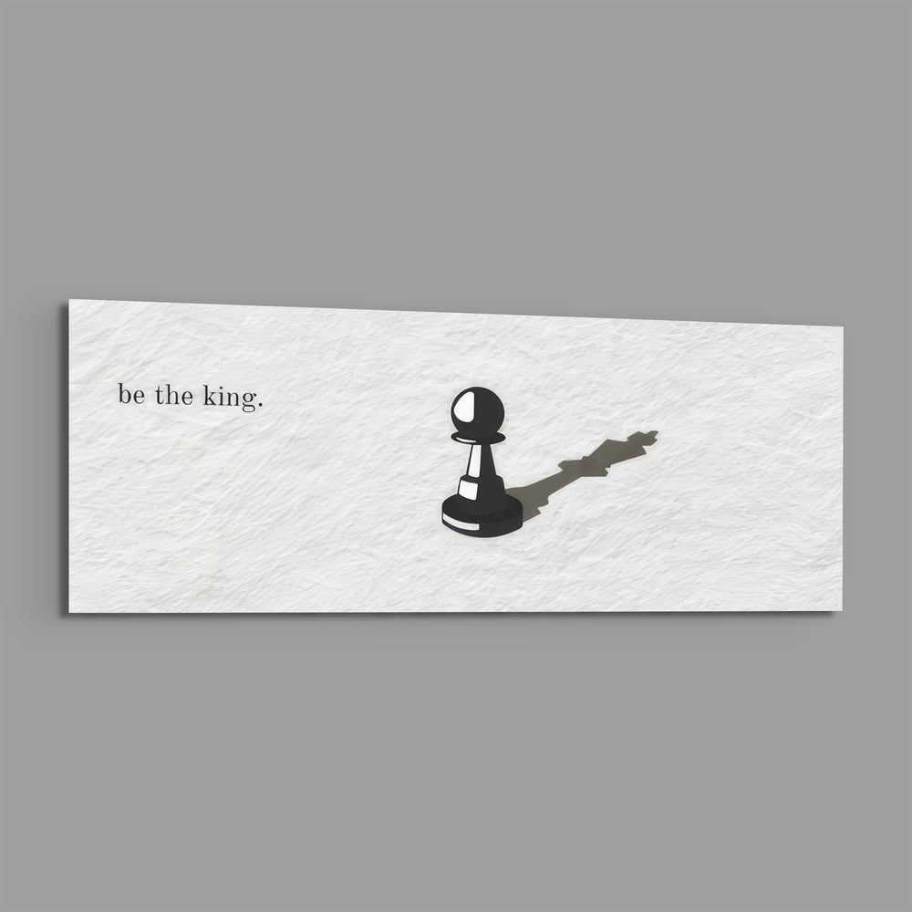 A single black chess pawn casting the long shadow of a king across a white textured surface, with a short motivational line of text panoramic glass wall art E