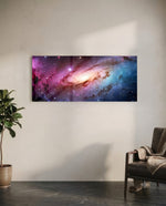 A glowing spiral galaxy swirling through clouds of pink, purple and blue across a star-filled cosmos. panoramic glass wall art C