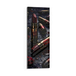 Dark, dramatic still life of crimson lipsticks shaped like brass cartridges, scattered with red lip prints, petals and water droplets. panoramic glass wall art D