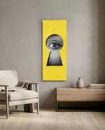 A black-and-white human eye peering out through a keyhole-shaped cutout in a flat, bright-yellow surface. panoramic glass wall art F