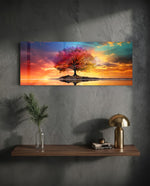 A lone tree with multicolored foliage standing on a small island, mirrored in still water beneath a fiery, cloud-swept sunset sky. panoramic glass wall art D