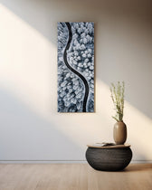 An aerial view of a dark, curving road snaking through a snow-covered pine forest in cool monochrome. panoramic glass wall art A