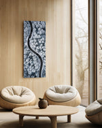 An aerial view of a dark, curving road snaking through a snow-covered pine forest in cool monochrome. panoramic glass wall art C