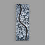 An aerial view of a dark, curving road snaking through a snow-covered pine forest in cool monochrome. panoramic glass wall art E