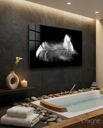 Feather glass wall art displayed above a soaking tub in a stone-tiled bathroom