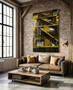 Yellow Stairs glass wall art displayed above a brown leather sofa in a brick-walled industrial lounge with gold cushions