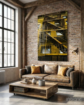 Yellow Stairs glass wall art displayed above a brown leather sofa in a brick-walled industrial lounge with gold cushions