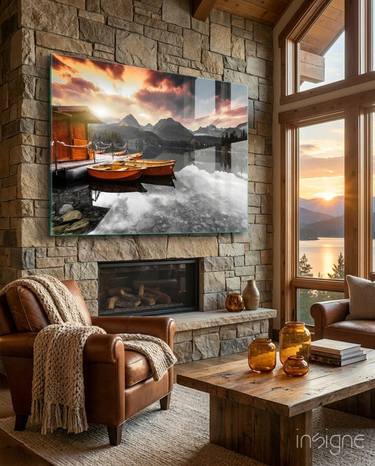 Sunrise Lake glass wall art displayed above a stone fireplace in a rustic stone-walled cabin lounge with brown leather chairs