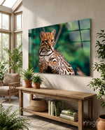 Ocelot Gaze glass wall art displayed above a wood console in a bright biophilic conservatory with rattan chair and ferns
